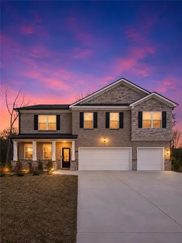 Brick and stone facade residence featuring a covered front porch with white columns, a dark panel front door, and a three-car garage