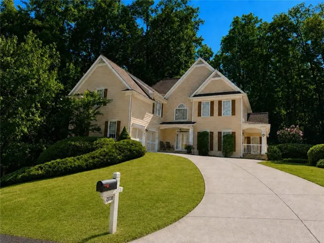 Two-story residence with light-colored siding and dark shutters, featuring a curved concrete driveway