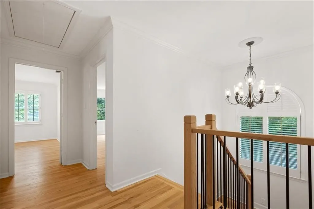 Hardwood flooring, wrought iron chandelier, arched window with louvered shutters, wooden stair railing with black spindles, and crown molding
