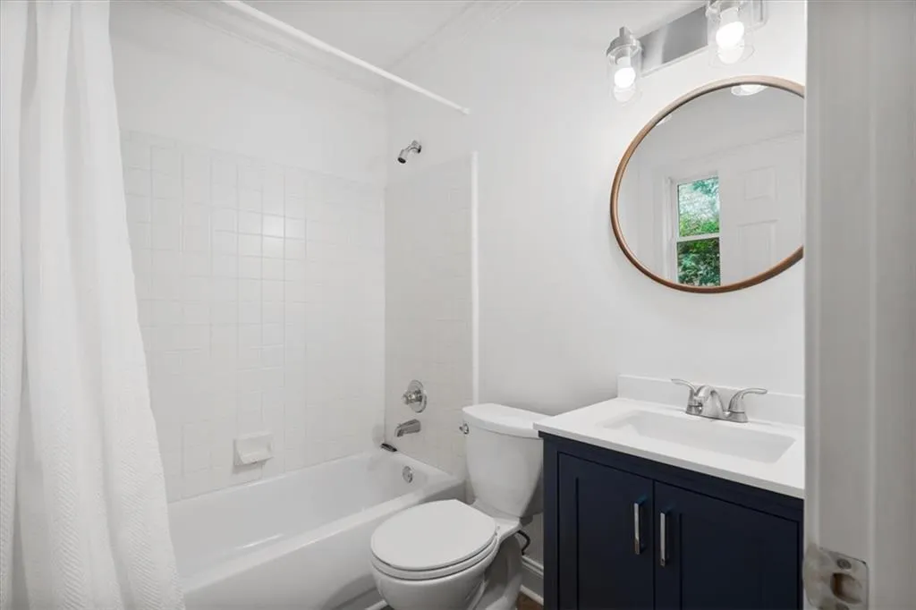 Lower level bathroom - White tile shower surround, chrome shower fixtures, white vanity with a dark blue cabinet, chrome faucet, and a round framed mirror