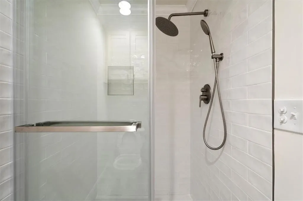 Primary Shower enclosure featuring clear glass panels, a brushed metal handle, and a built-in shelf