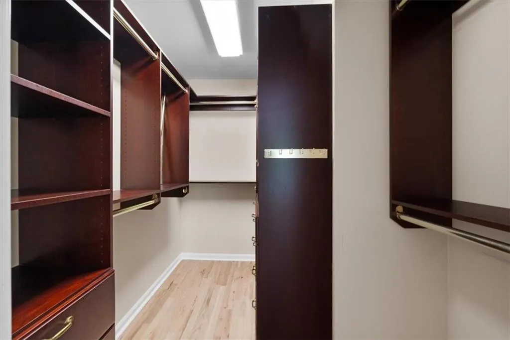 Primary Bedroom Custom closet system featuring dark wood-finish cabinetry, integrated shelving, and brass-tone hardware