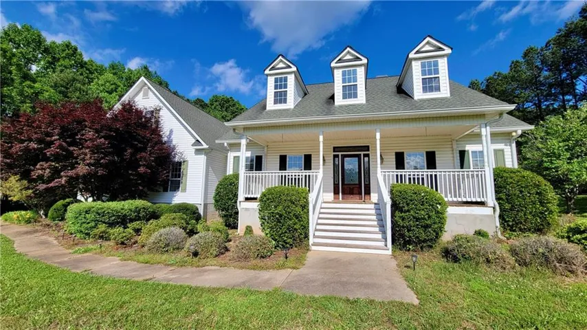 White siding exterior with a covered front porch, white railings, and three dormer windows