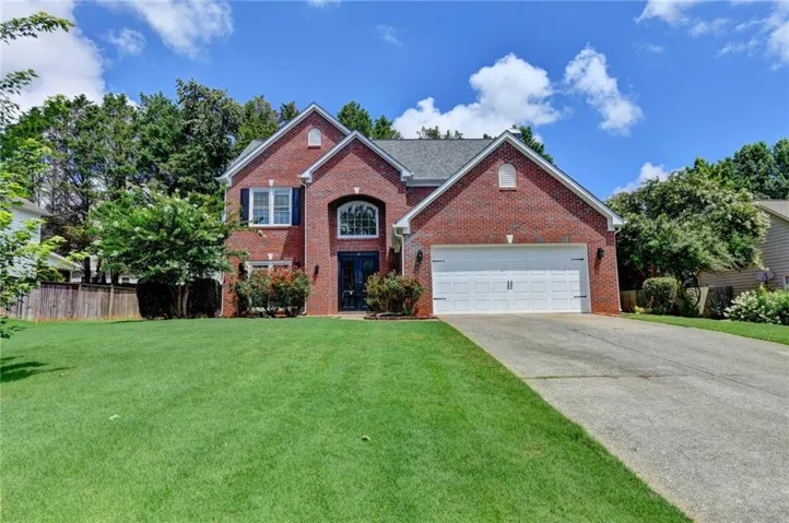Traditional brick exterior featuring a multi-pane arched window, black double-door entry, a two-car garage, and a concrete driveway
