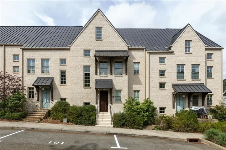 Multi-level townhome architecture featuring a light-colored brick facade, dark metal roofing, and multiple gables