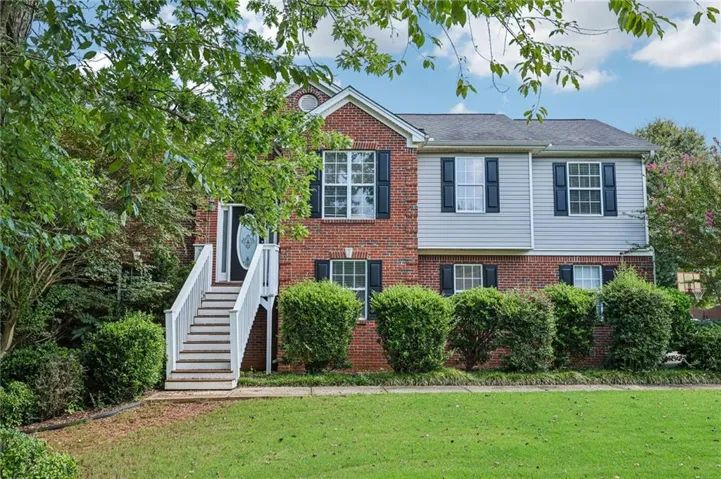 Brick and siding exterior with dark shutters, featuring a prominent front entrance with a decorative glass door, elevated by a white-railed staircase