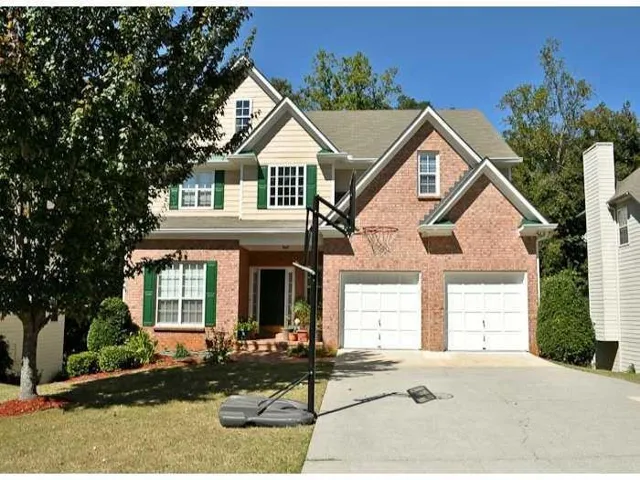 Brick and siding exterior with a gabled roofline, featuring a two-car garage, multiple windows with shutters, and mature landscaping