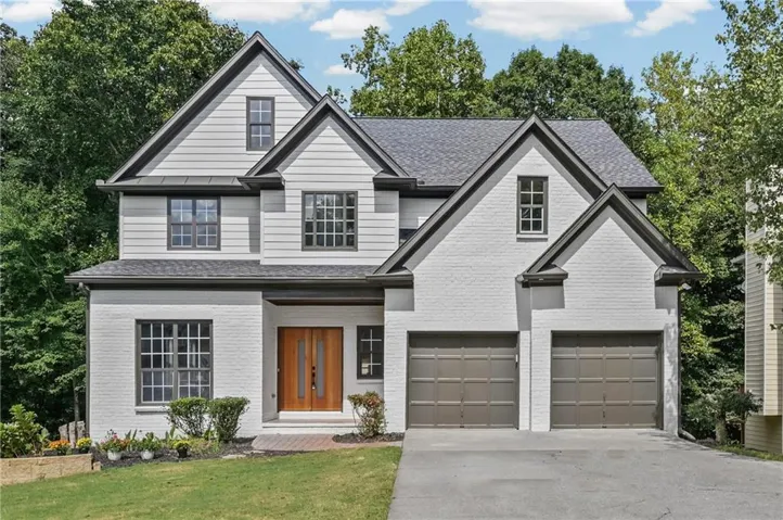 Two-story exterior with a mix of white painted brick and horizontal siding, featuring a wood double-door entry, a two-car garage, and dark-framed windows
