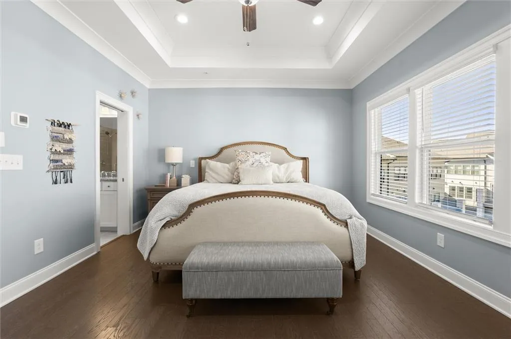 Bedroom featuring wood-type flooring, ornamental molding, ceiling fan, ensuite bath, and a raised ceiling