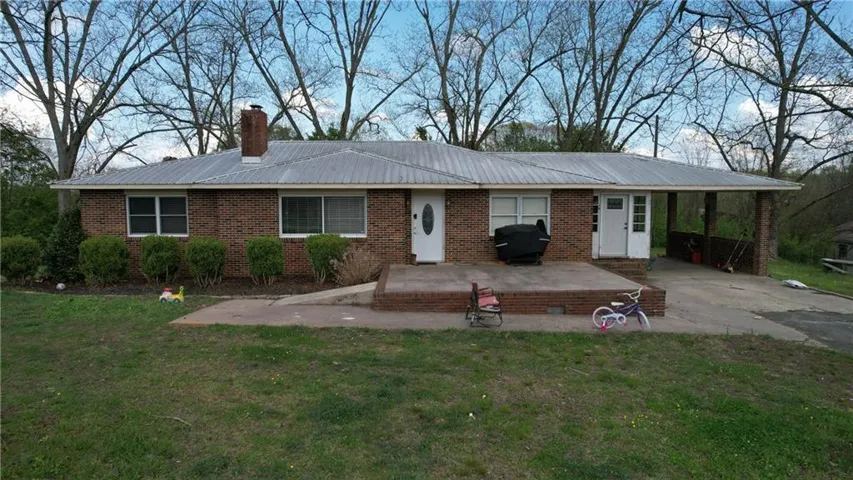 Brick exterior featuring a metal roof, front concrete patio, and a covered carport