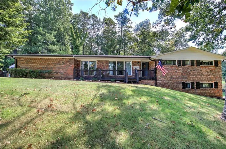 Brick exterior with a gabled roofline, front porch with black railing, and mature trees surrounding the property