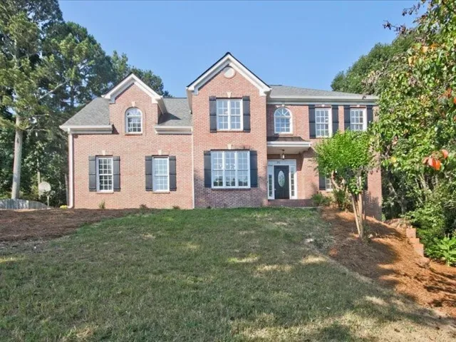 Brick exterior featuring a gabled roofline, multiple dormers, and black louvered shutters