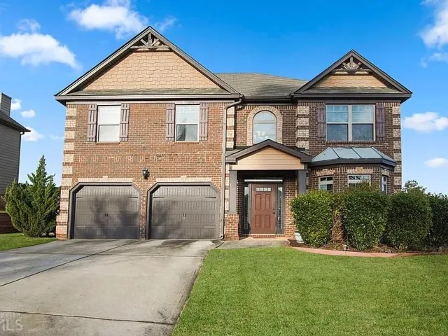 Brick facade residence featuring a two-car garage, established front landscaping, an arched window accent, a bay window, and a covered entry
