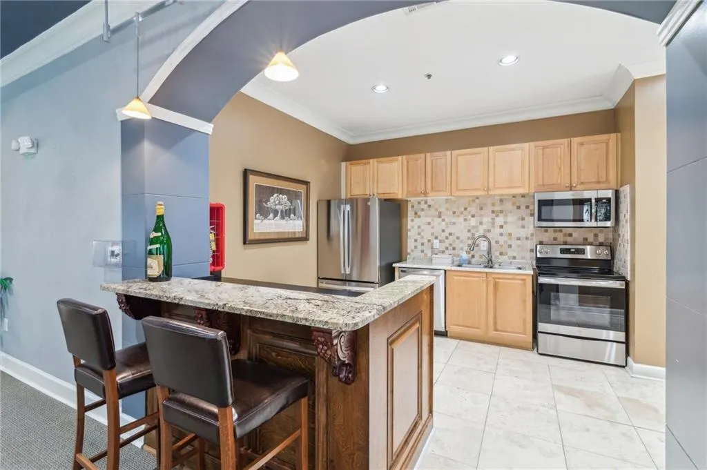 Lobby/Community Kitchen featuring stainless steel appliances, light brown cabinets, a sink, crown molding, and decorative backsplash