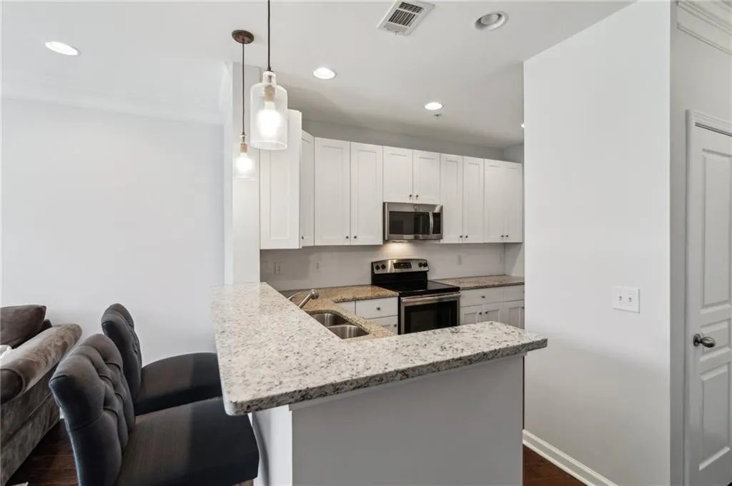 Kitchen with appliances with stainless steel finishes, a sink, dark wood finished floors, recessed lighting, and light stone counters