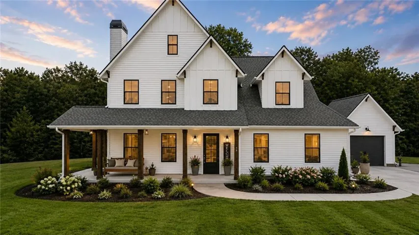 Modern farmhouse exterior featuring white board-and-batten and horizontal siding, a dark shingle roof, a covered front porch with substantial wood posts, black-framed windows, and an attached two-car garage with a dark door