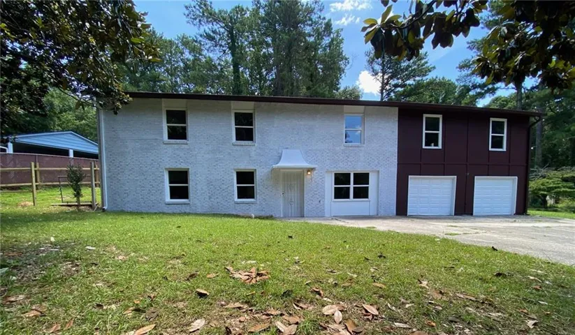 Two-story exterior featuring a textured light-colored facade with contrasting dark panels, multiple windows, and two garage doors