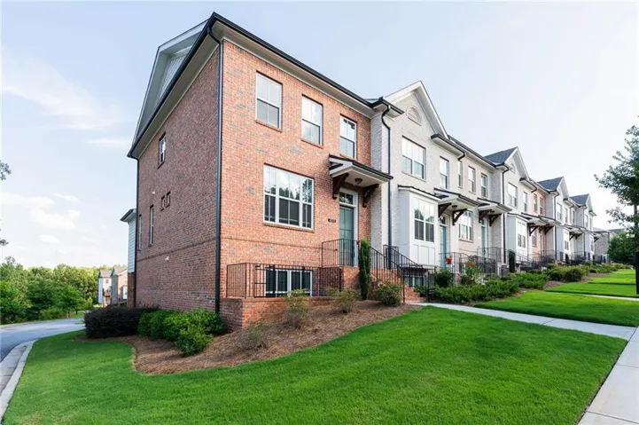 Brick and painted brick townhome with black trim, multiple windows, and a landscaped front yard with a concrete sidewalk