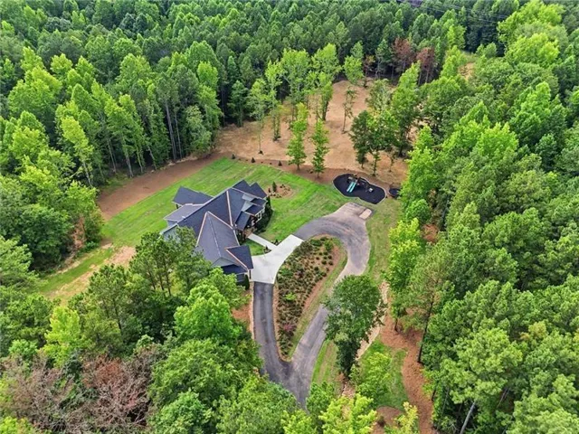 Spacious property featuring a large residence, winding paved driveway, expansive lawn areas, and mature surrounding tree cover