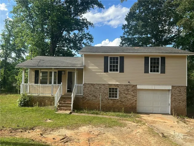 Split-level residence featuring a covered front porch with white railings, a tan siding upper level with dark shutters, and a brick lower level