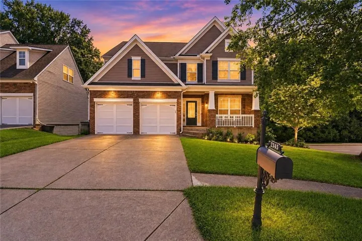 Two-story residence featuring a two-car garage, brick and siding exterior, front porch with white railing, and a concrete driveway