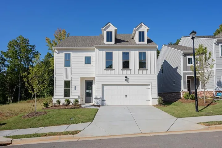 White siding exterior with a dark gray front door, two dormer windows, an attached two-car garage, and a concrete driveway