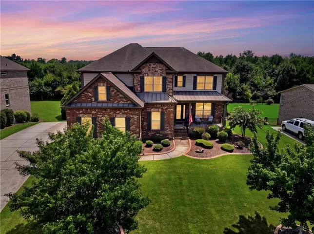 Brick and stone exterior with dark shutters, front porch, mature landscaping, and an expansive lawn