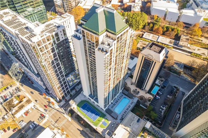 High-rise building with a green pyramidal roof, featuring a ground-level tennis court and two swimming pools