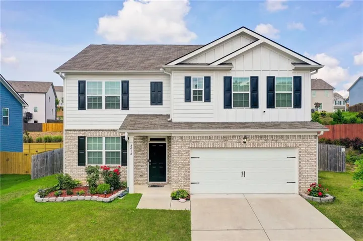 Two-story residence featuring a white siding and light brick facade, dark shutters, an integrated garage, a concrete driveway, and a manicured front lawn with established landscaping