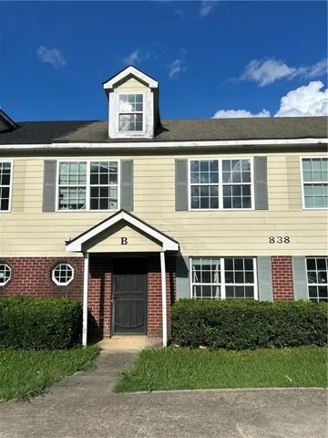 Multi-level townhome featuring a dormer window, light-colored siding, and a brick facade
