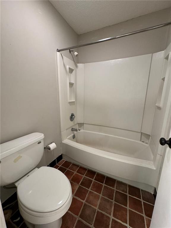 Bathroom featuring a textured ceiling, shower / bath combination, toilet, and tile flooring
