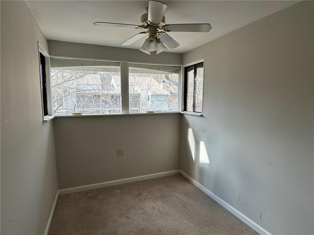 Empty room with a wealth of natural light, light carpet, and ceiling fan