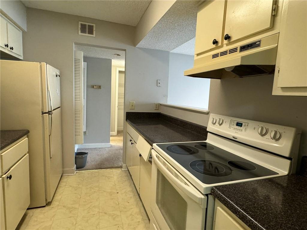 Kitchen with white cabinetry, a textured ceiling, white appliances, and light tile floors