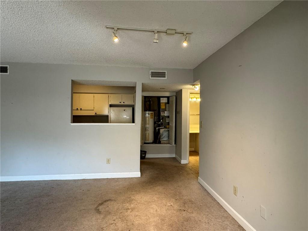 Empty room with rail lighting, light carpet, electric water heater, and a textured ceiling