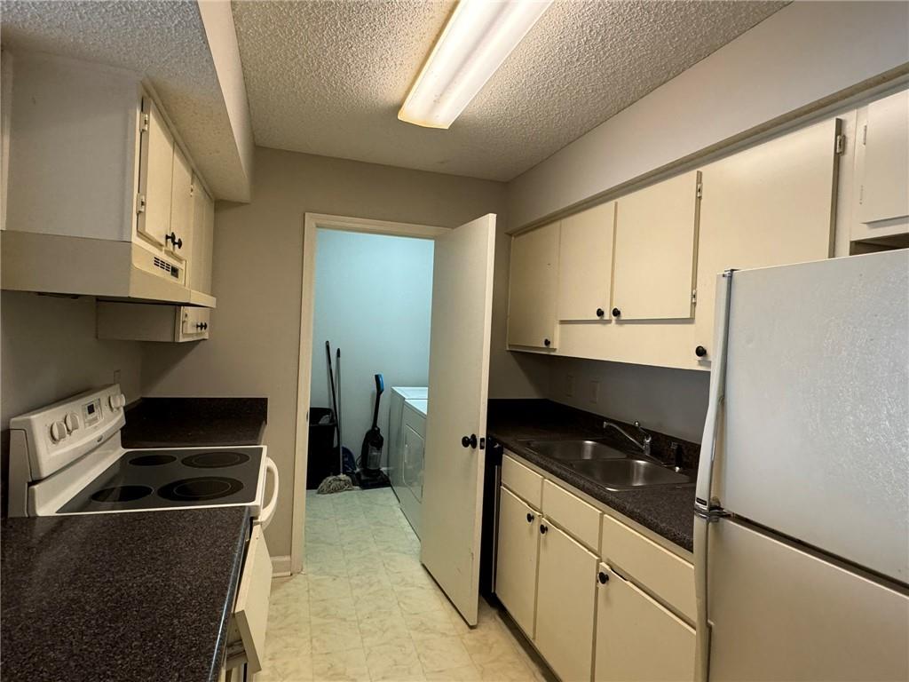 Kitchen featuring light tile flooring, white appliances, a textured ceiling, sink, and white cabinetry