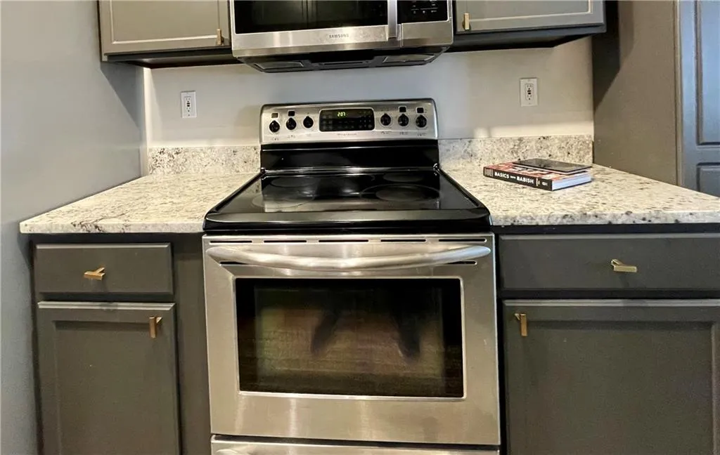 Kitchen with gray cabinets, stainless steel appliances, and light stone counters