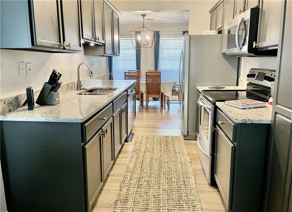 Kitchen with sink, a notable chandelier, light wood-type flooring, hanging light fixtures, and stainless steel appliances