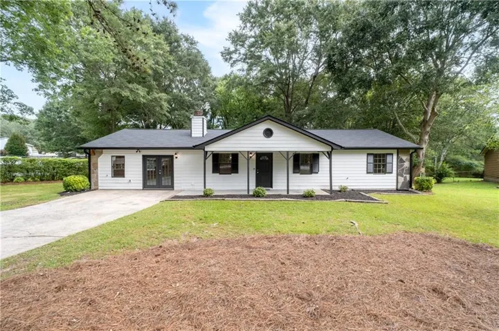 White exterior siding with stone accents, black roof, covered front porch, and mature trees
