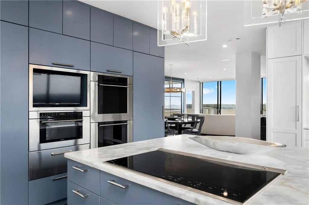 Kitchen with blue cabinetry, black electric stovetop, hanging lights, and stainless steel double oven