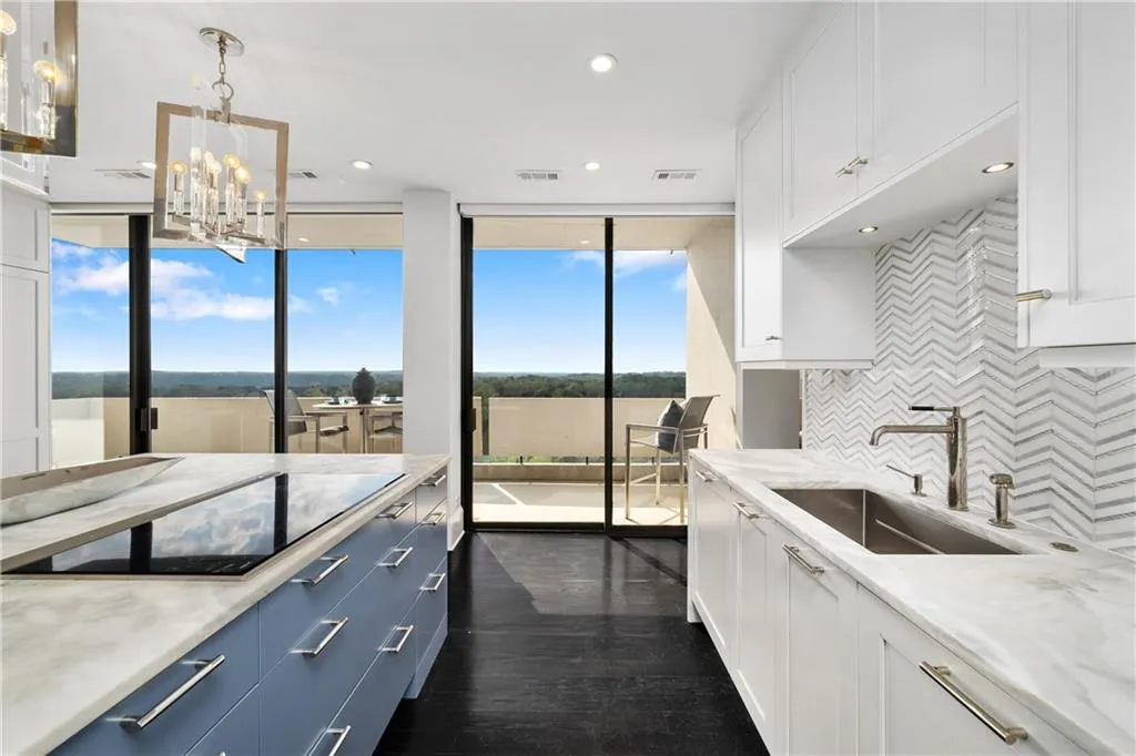 Dual tone kitchen featuring light stone counters, black electric cooktop, dark wood-type flooring, hanging lights, and decorative backsplash