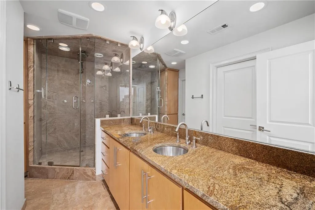 Full bath with double vanity, a marble finish shower, and recessed lighting