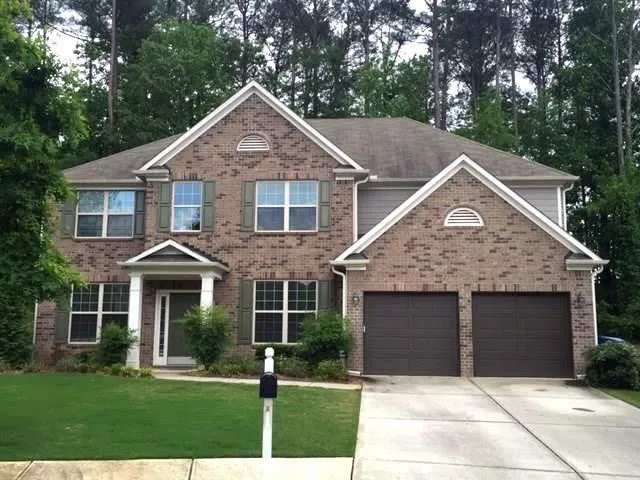 Brick facade residence featuring a covered entry, two-car garage, manicured lawn, and mature trees