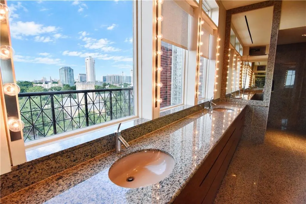 Elongated vanity with integrated sinks, polished stone countertop, wood-finish cabinetry, and extensive mirrored surfaces with integrated lighting