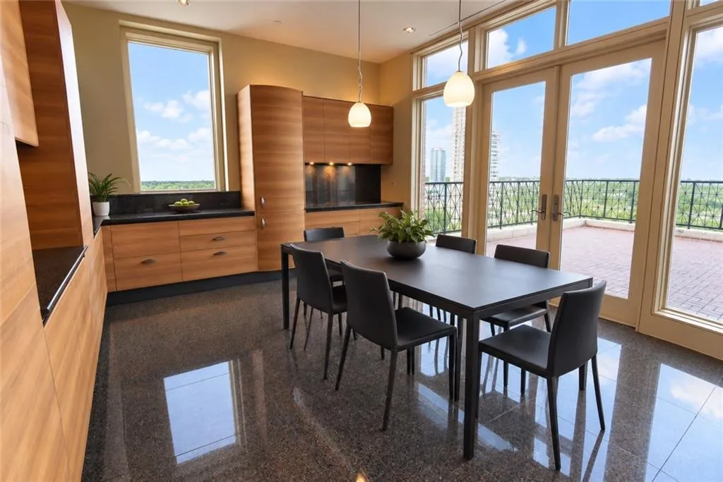 Sleek wood-finish cabinetry with black countertops, polished dark flooring, and floor-to-ceiling glass doors opening to a large outdoor patio with brick pavers and a dark metal railing