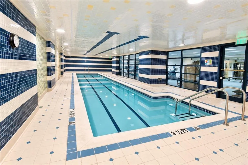 Indoor lap pool with blue and white mosaic tile walls, white tile flooring with blue accents, and recessed ceiling lighting