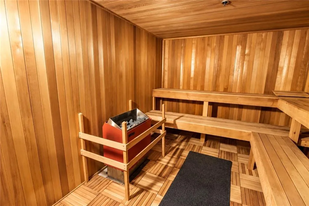 Wood-paneled sauna with built-in wooden benches, a sauna heater, and wood-tile flooring