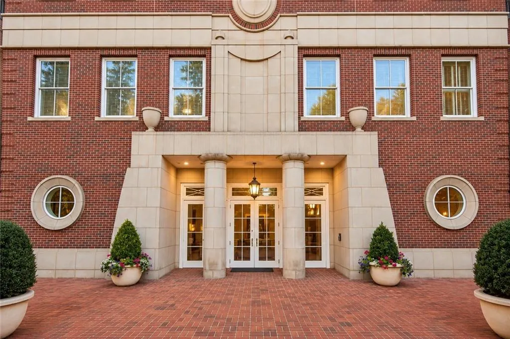 Brick exterior with stone accents, round windows, a covered entry with columns, and a paved brick forecourt