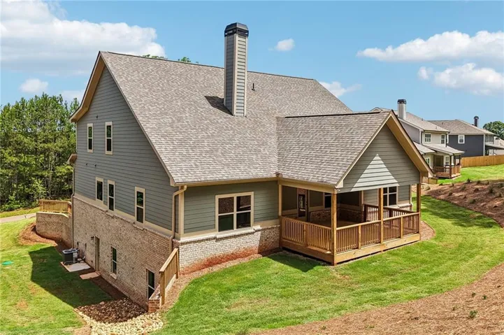 Rear exterior featuring a covered porch with natural wood railing, multi-story design, brick and siding facade, and a chimney