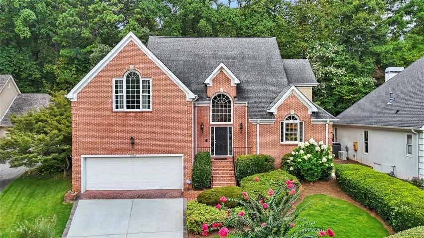 Brick exterior with multiple gables, arched windows, an integrated two-car garage, and established landscaping