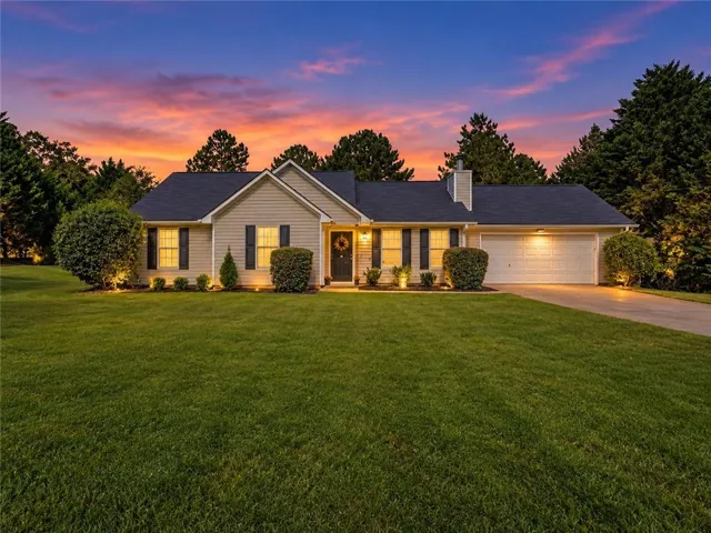 Cream-colored siding residence featuring a dark shingle roof, attached two-car garage, concrete driveway, and a manicured front lawn